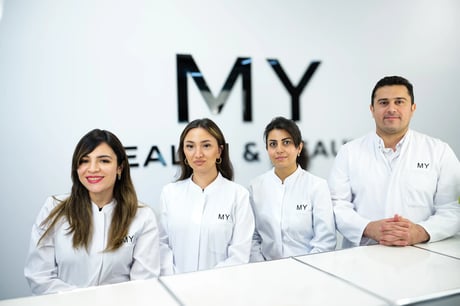 Four medical professionals in white coats stand smiling before a 'MY HEALTH & BEAUTY' sign.