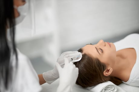 Woman receiving a hair restoration treatment on her scalp from a technician.